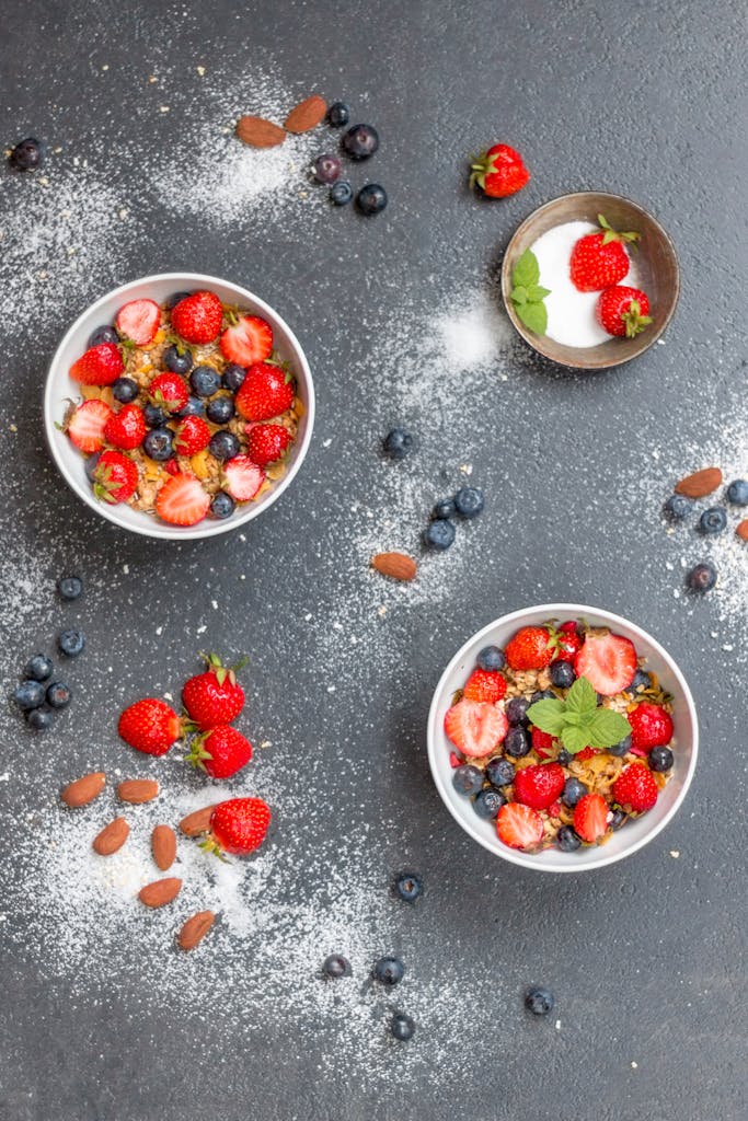 Sobre Nosotros 7 Top view of bowls filled with cereal, strawberries, and blueberries, perfect for a healthy breakfast.